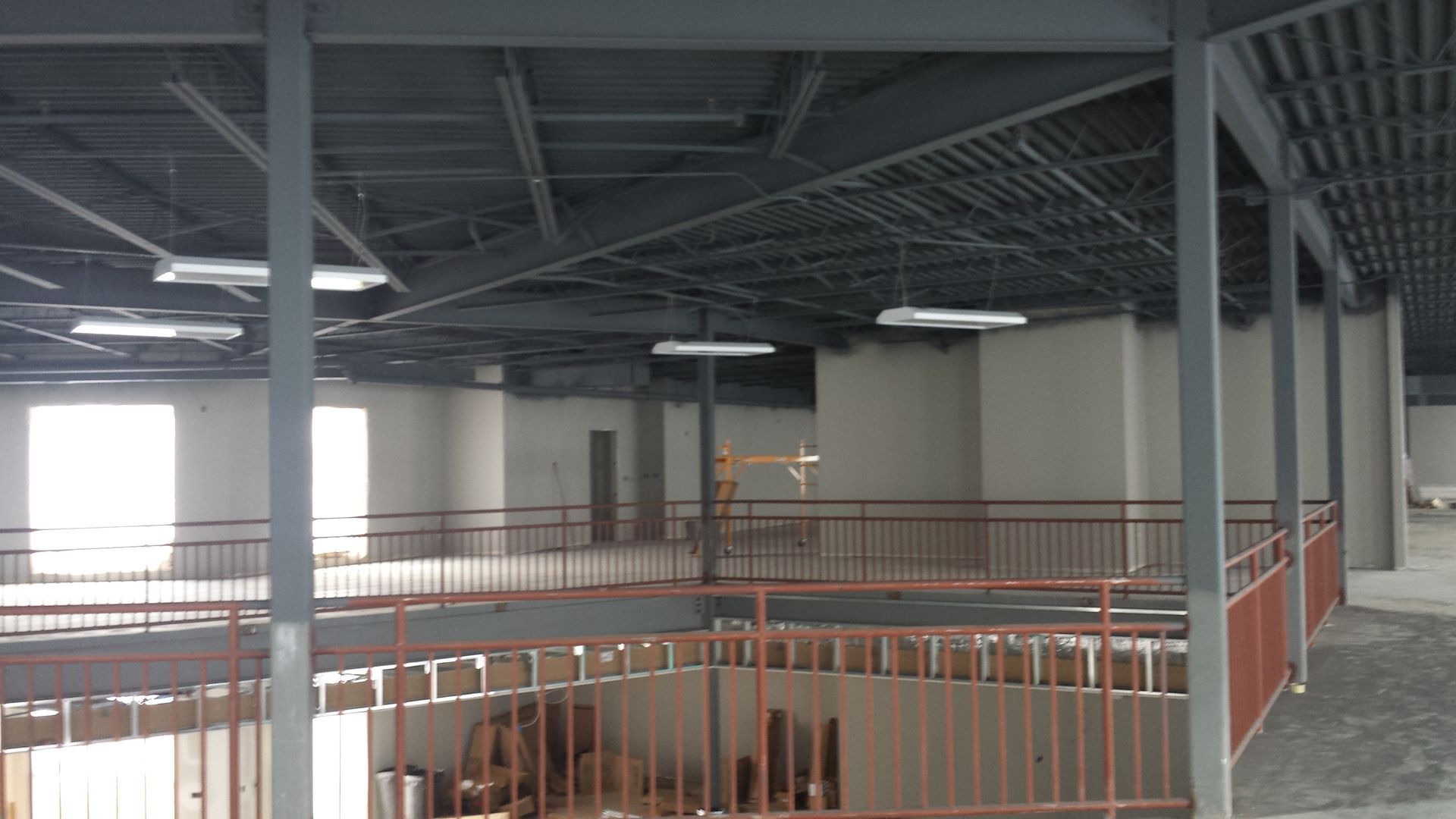 Interior of an empty industrial building with metal railings, steel beams, and large windows.