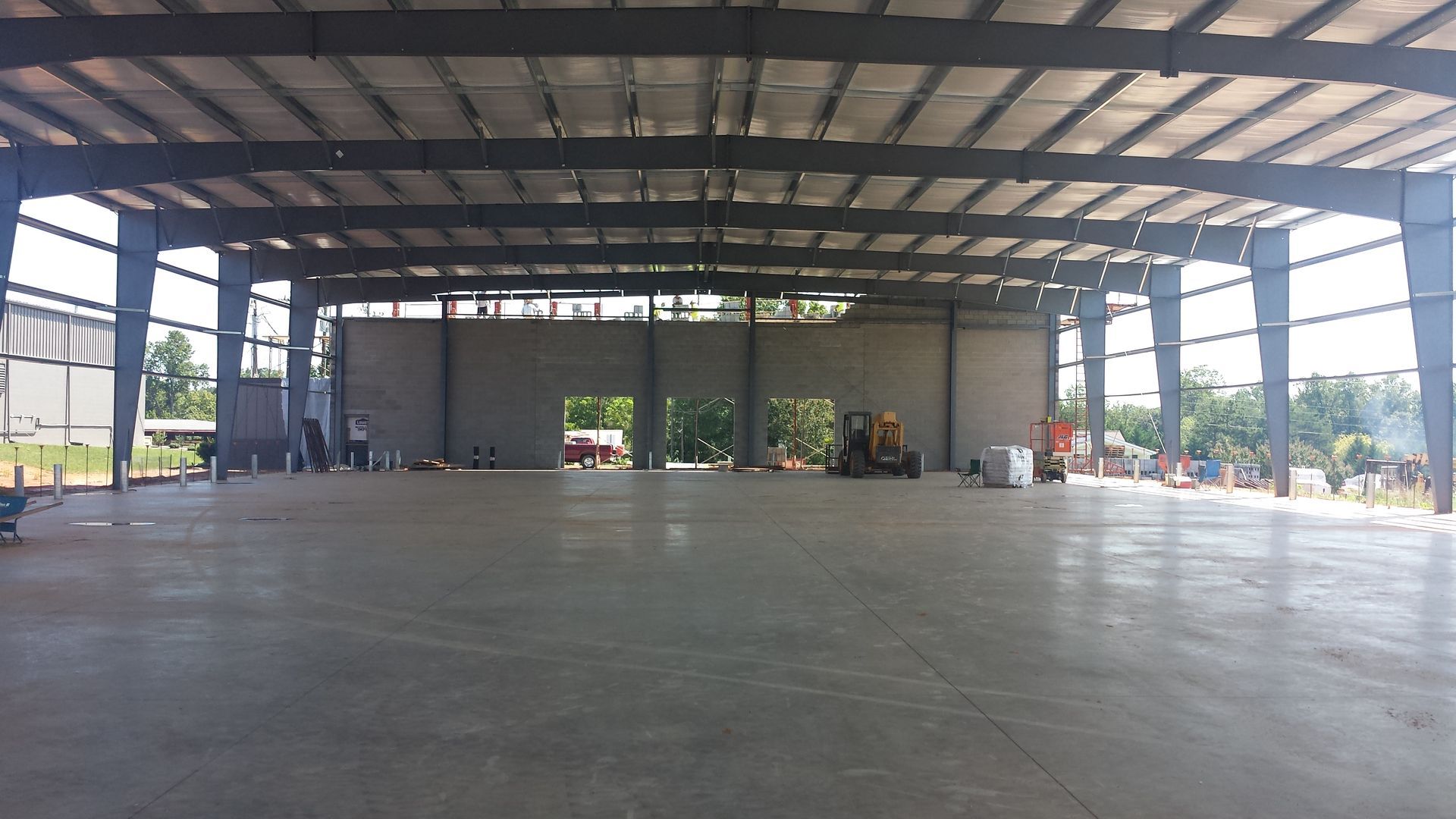 Empty indoor warehouse with a concrete floor and steel roof structure, open bays in the distance