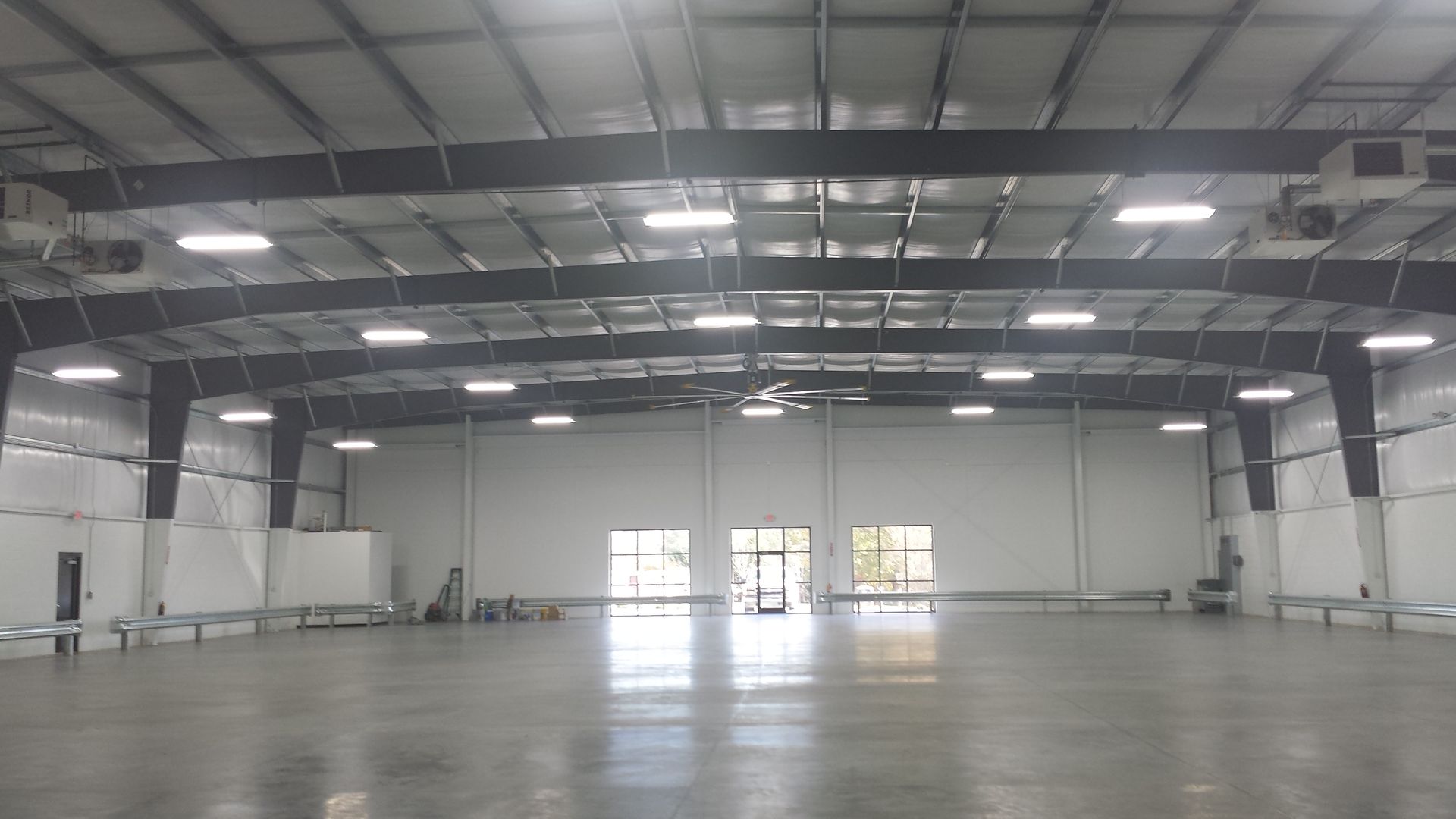 Empty industrial warehouse interior with high ceiling, exposed beams, and large open concrete floor.