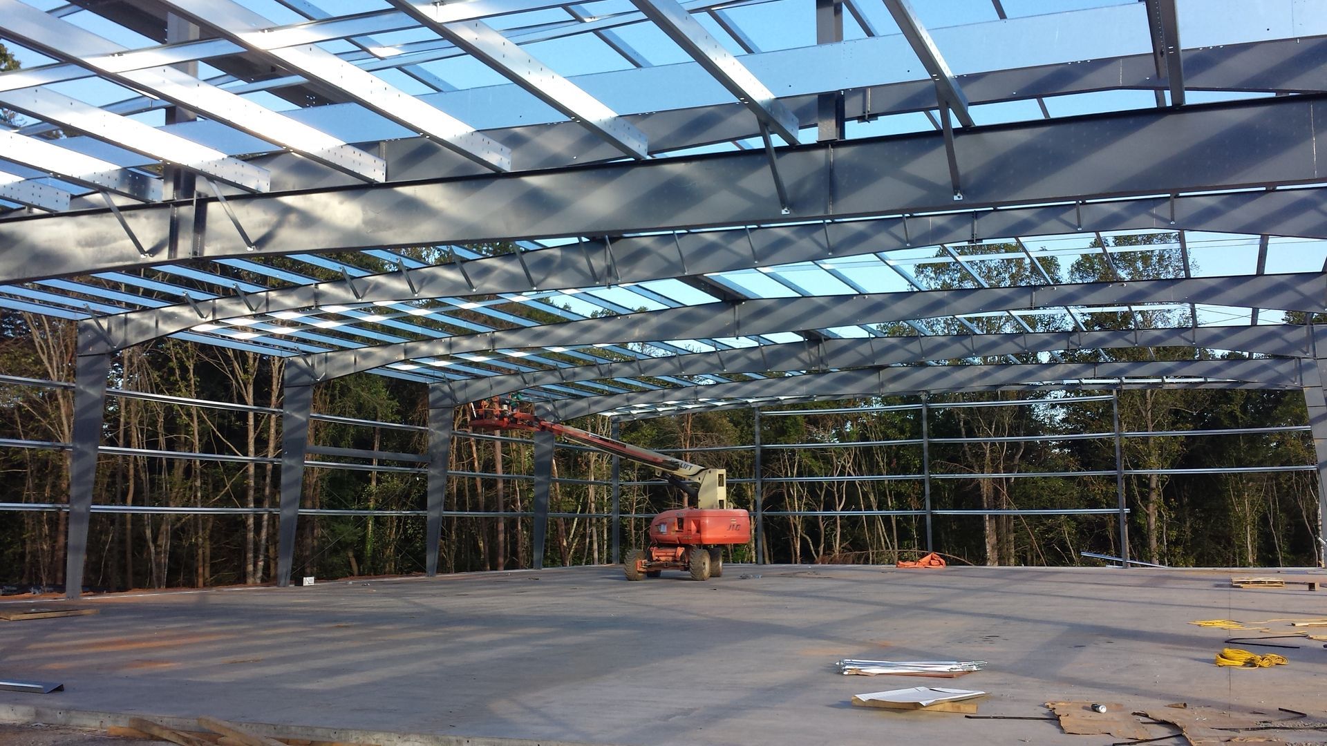 Steel frame building under construction with a small orange lift in an open, partly roofed structure