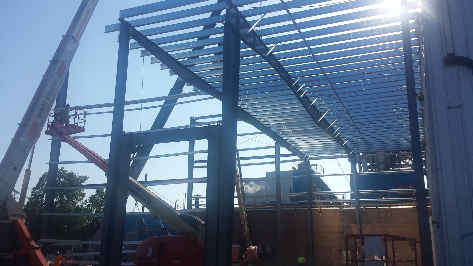 Steel frame building under construction with red lift equipment and sunlit roof beams
