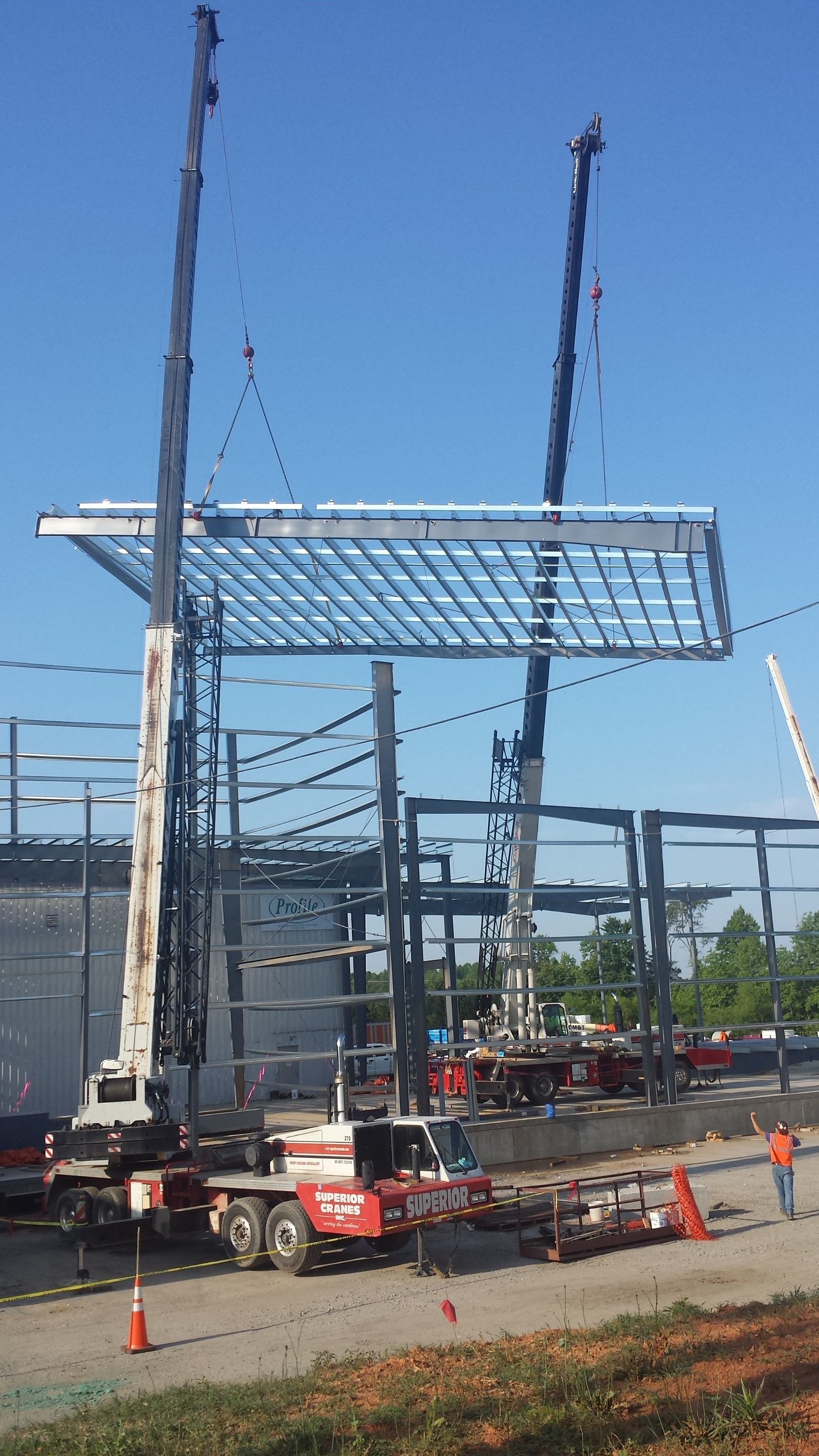 Construction site with cranes lifting a steel roof frame onto a building skeleton