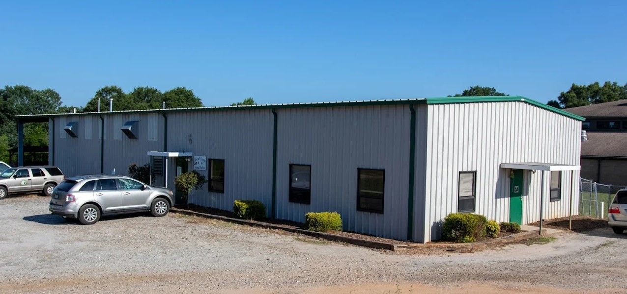 Gray metal industrial building with parked cars and gravel lot on a sunny day