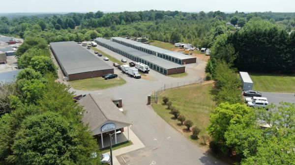 Aerial view of a low-rise industrial complex with parked vehicles, trees, and surrounding greenery