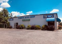 Carter’s Auto Shop building with blue awning, shrubs, and parking lot under a bright sky