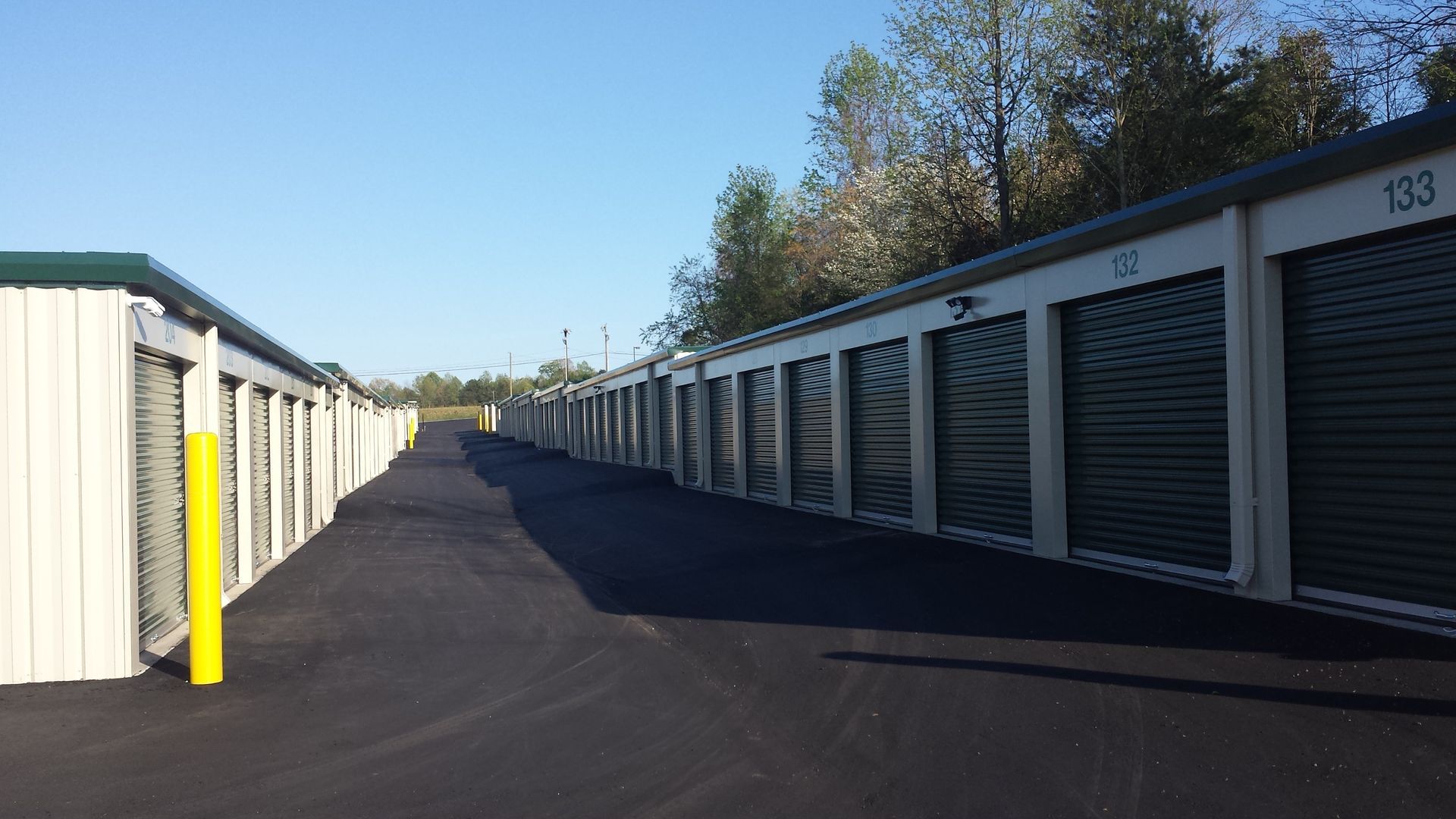 Row of white and gray storage units along a paved lane under a clear blue sky