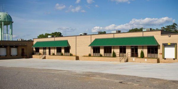 Single-story beige building with green awnings beside an empty parking lot under a blue sky