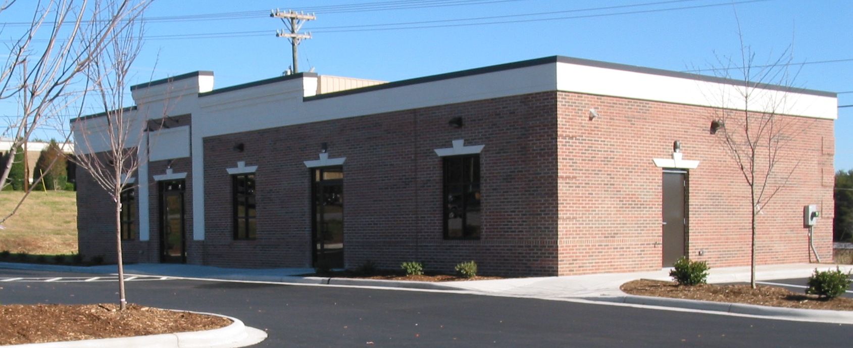 Brick utility building with dark trim, blacktop lot, and a clear blue sky