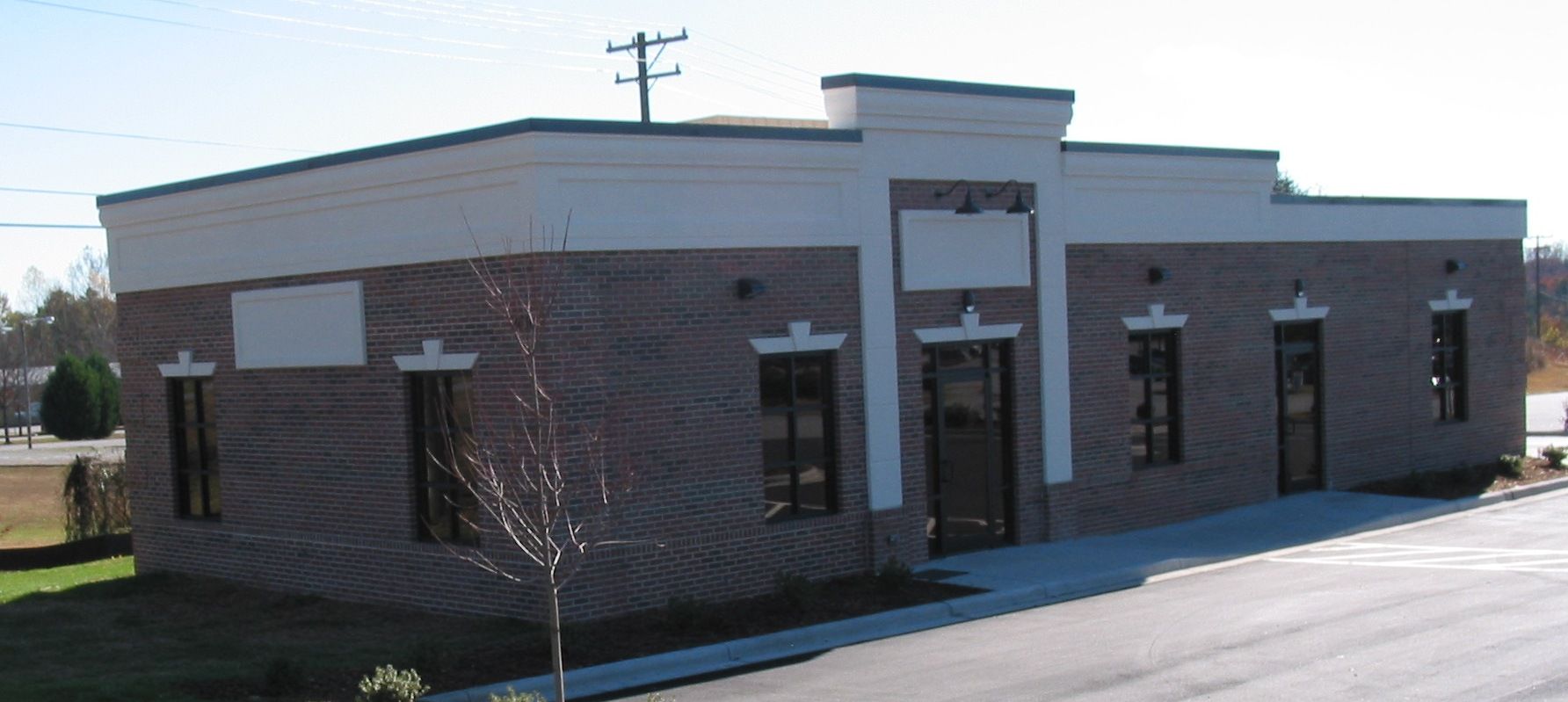 Small brick commercial building with dark windows and a light gray roof beside a road