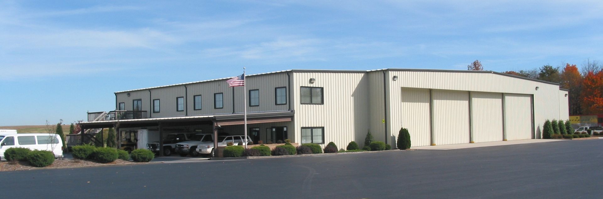 Low-rise industrial building with beige walls and a large parking lot under a clear blue sky