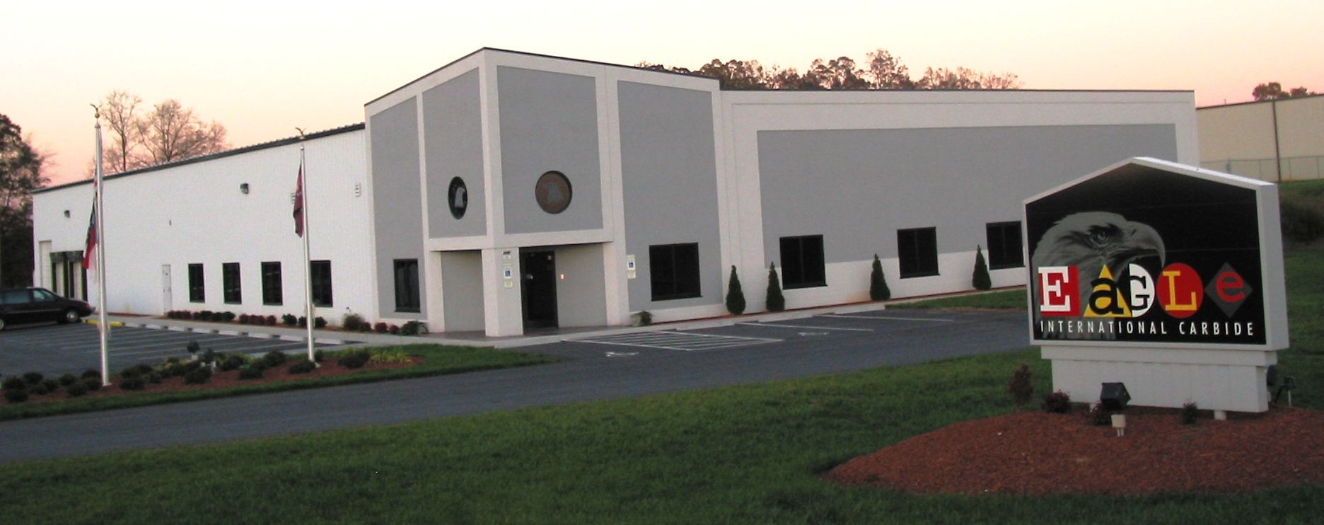 Modern white-and-gray office building with a colorful sign at the entrance during sunset