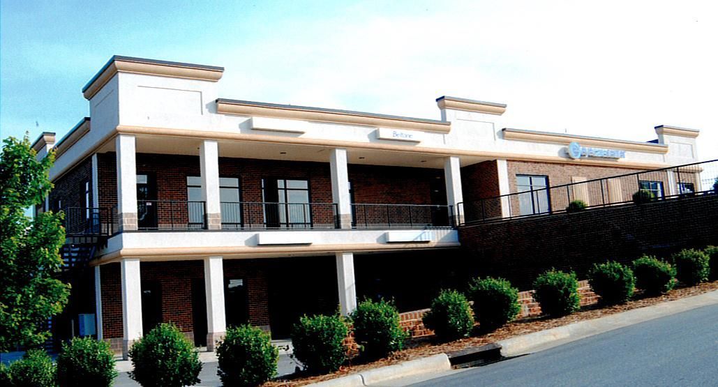 Two-story building with white columns and a hedge-lined front along a road