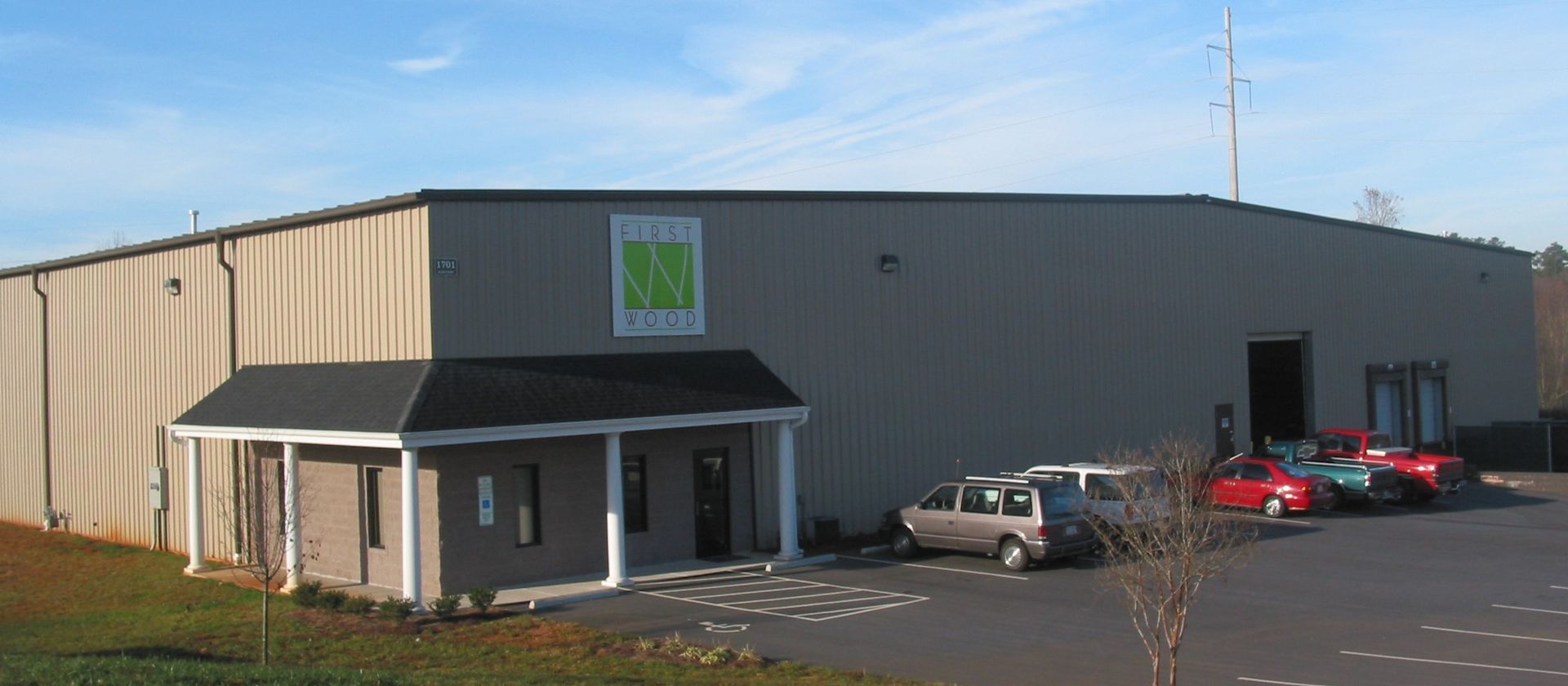 Industrial building with a small entrance porch and several parked cars in front