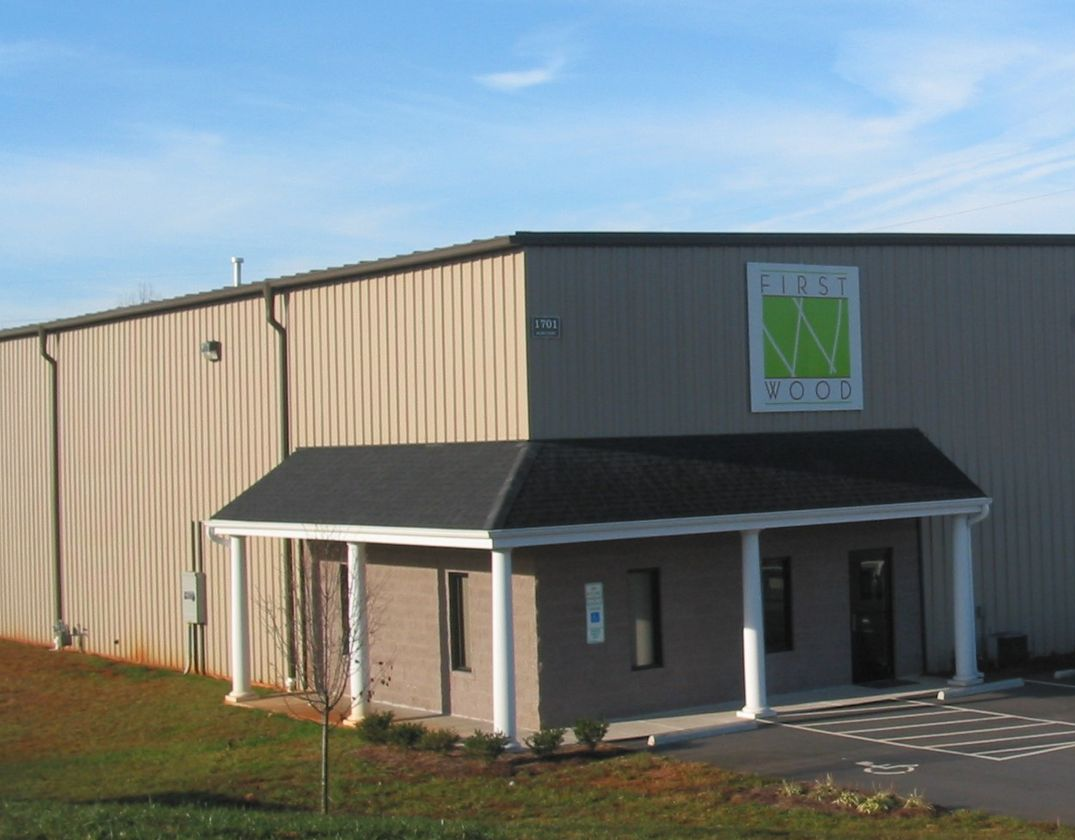 Small beige industrial building with a dark roof and covered entrance under a blue sky