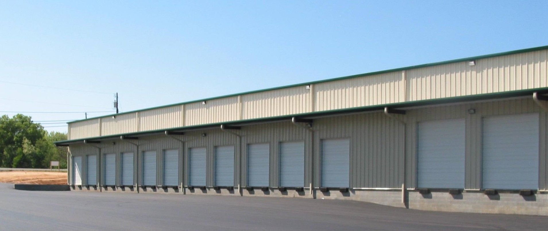 Row of closed gray loading dock doors on a beige industrial warehouse under a clear blue sky