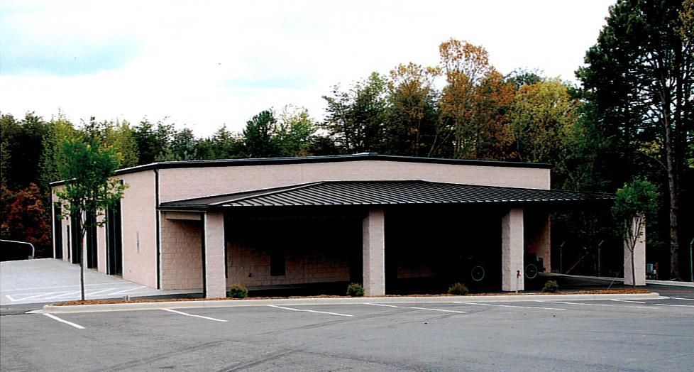 Single-story beige building with covered entrance and columns, surrounded by trees and empty parking lot