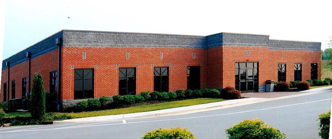 Brick office building with black-trimmed windows and landscaped frontage beside a road
