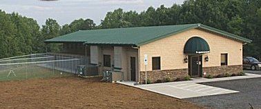 Small tan building with green roof beside a fenced field on a cloudy day