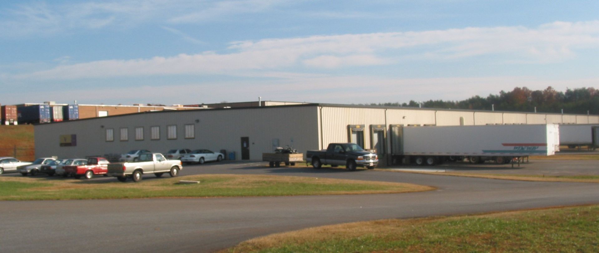 Industrial warehouse buildings with parked vehicles beside a road under a blue sky