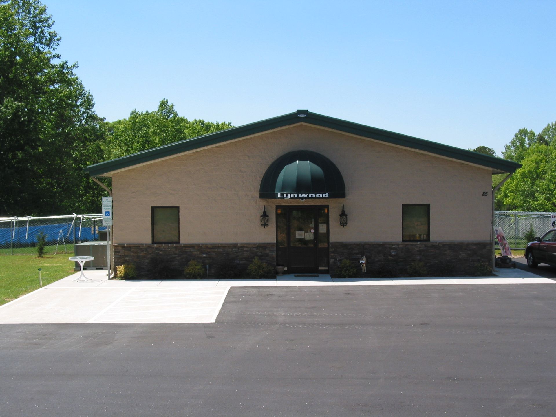 Small beige building with a green roof and arched entrance, viewed from a paved lot