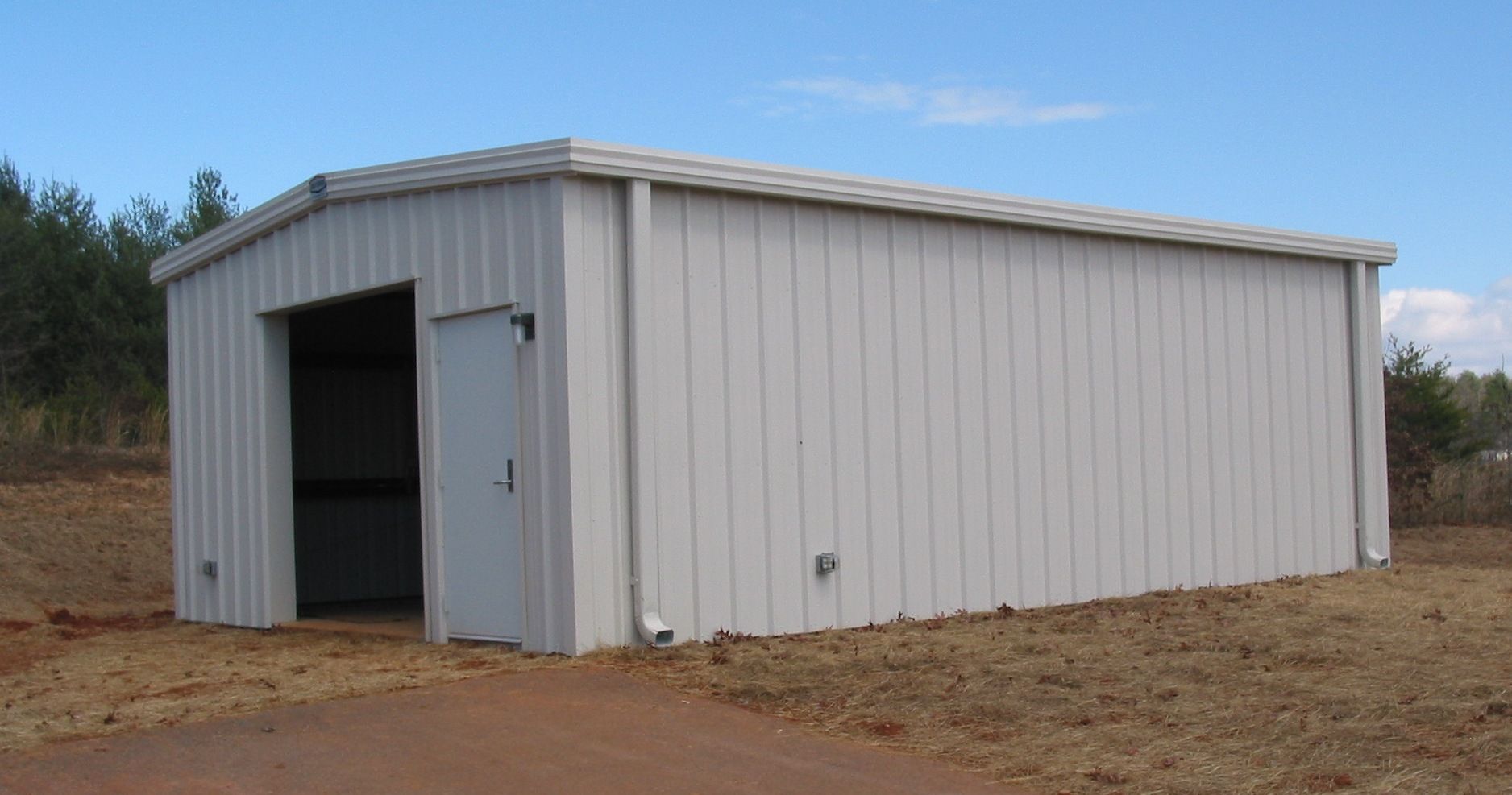 White metal storage shed with an open doorway on a dirt lot