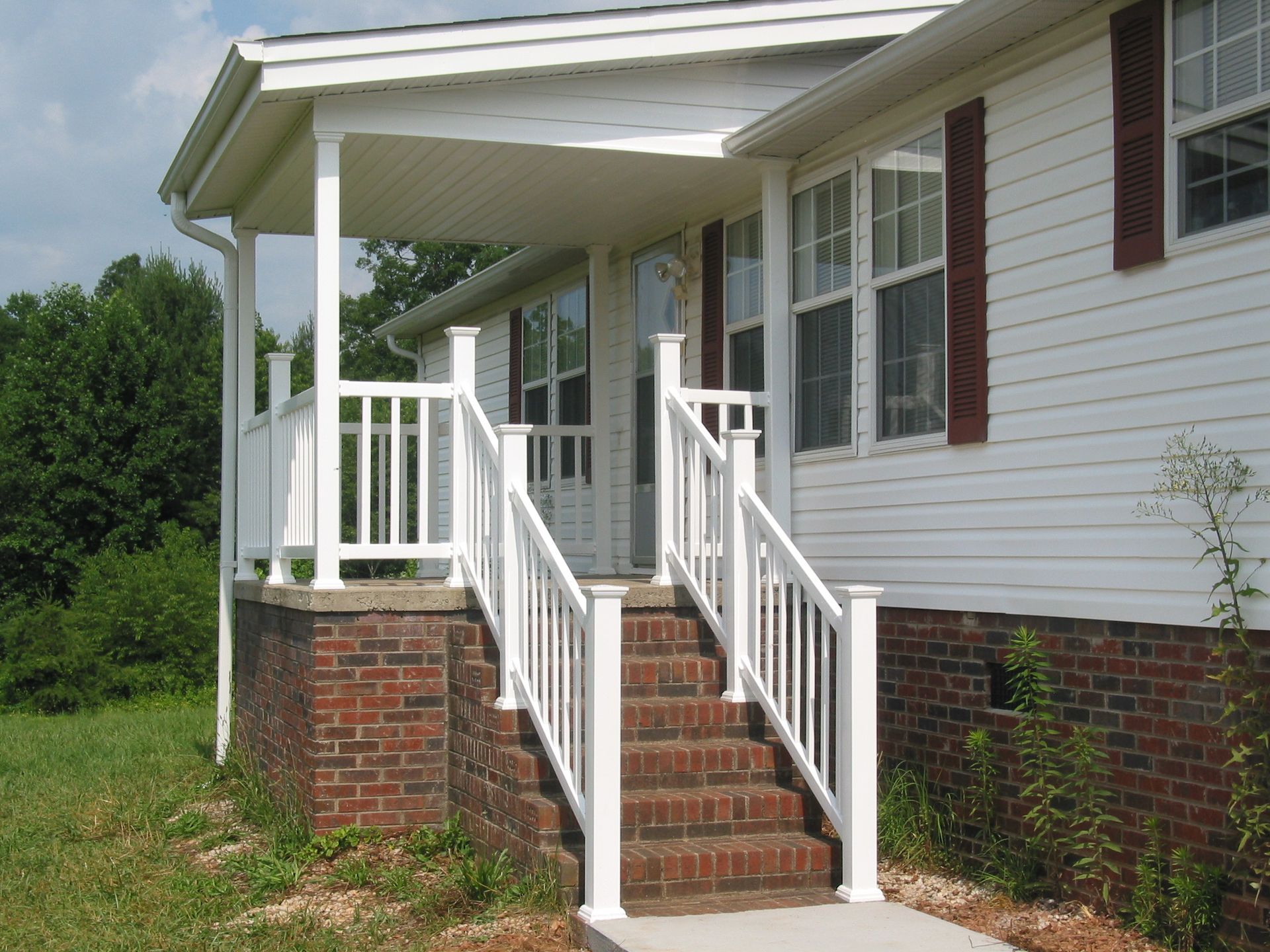 Front porch with brick steps, white railings, and a white-sided house exterior