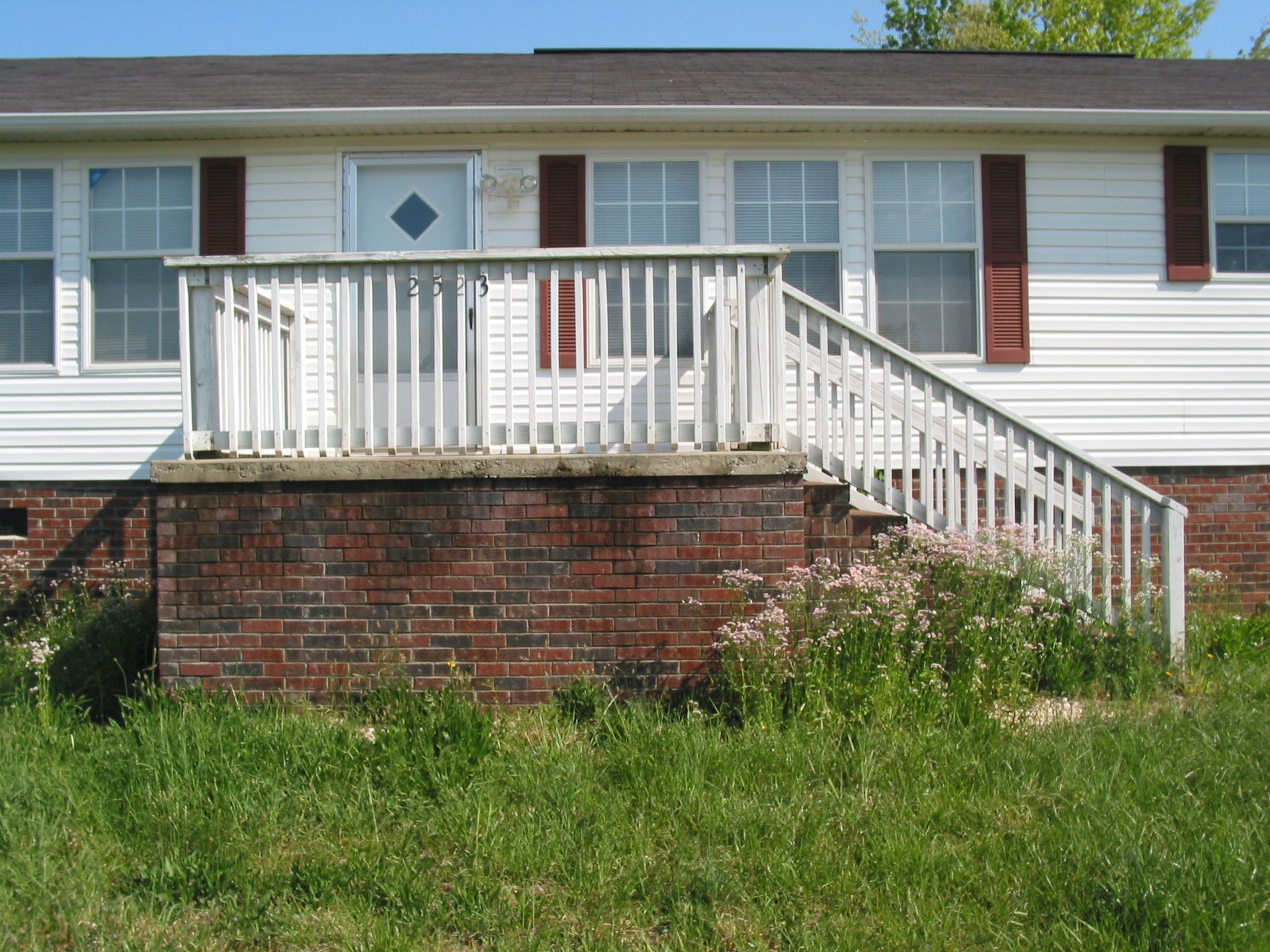 White front porch with stairs on a brick foundation, set against a grassy yard and blue sky