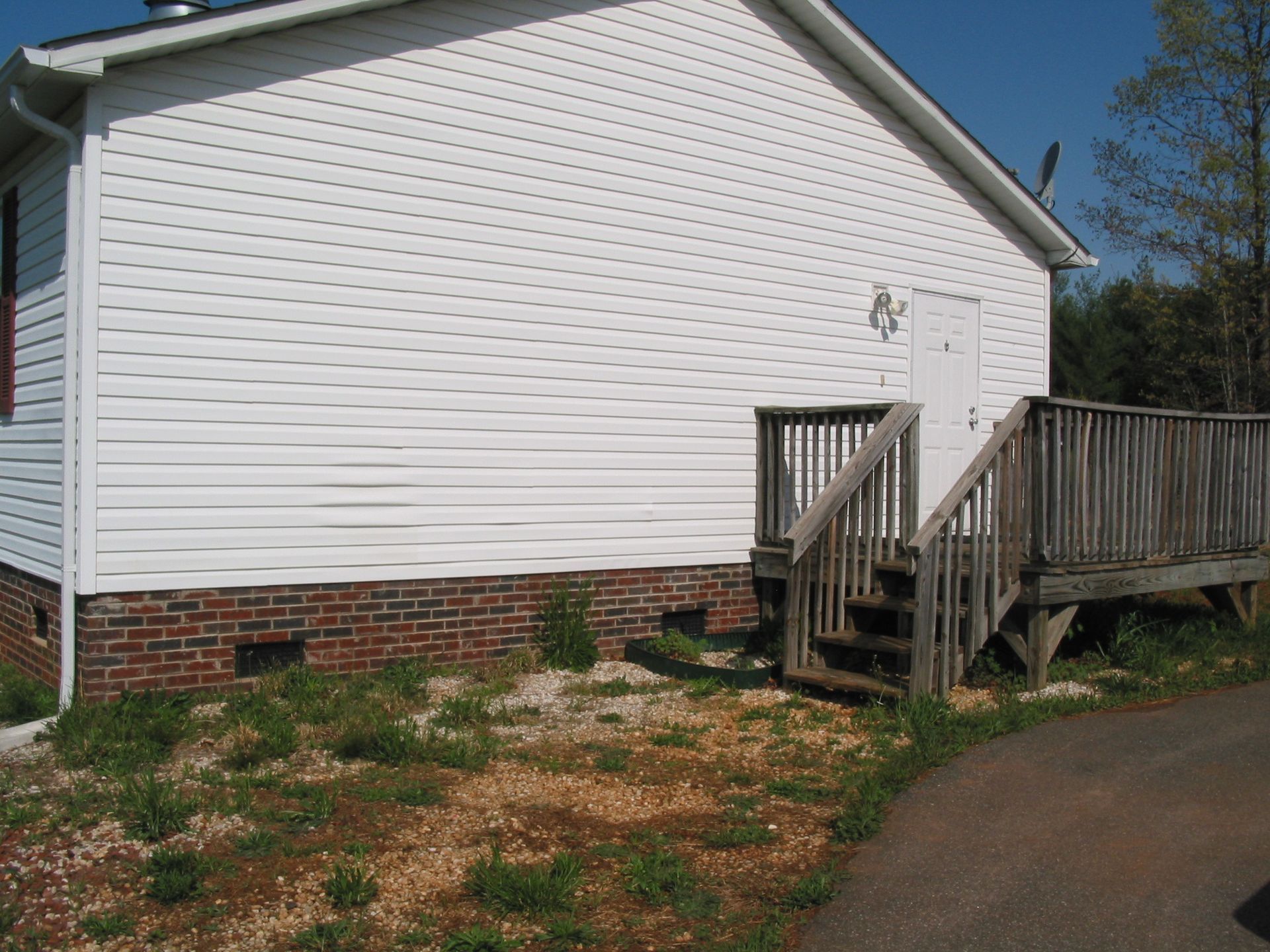 White vinyl house exterior with brick foundation, wooden steps, and driveway beside it