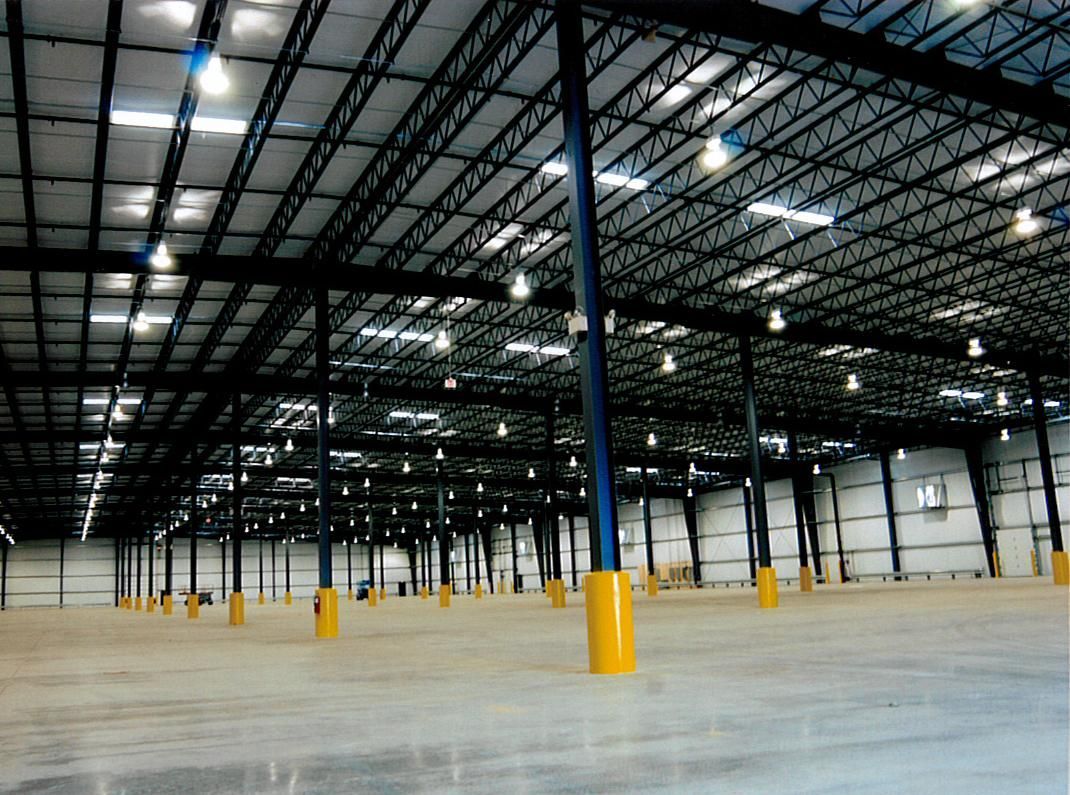 Empty warehouse interior with tall steel beams, concrete floor, and yellow safety columns