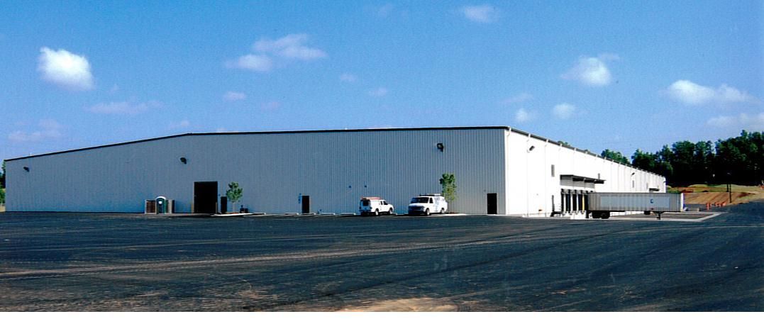 Large white warehouse building on a gravel lot under a blue sky