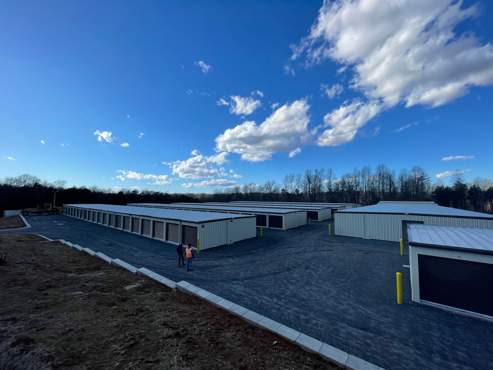 Wide gravel lot with rows of white storage containers under a bright blue sky with clouds