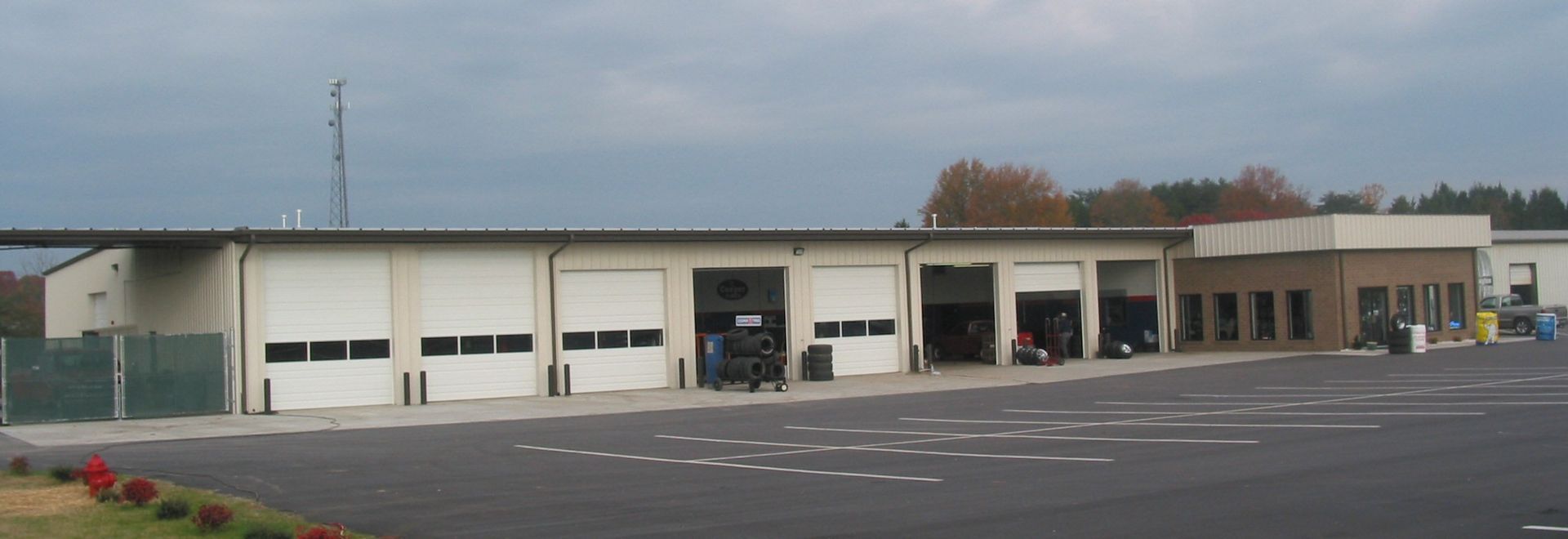 Wide beige storefront with garage doors and empty parking lot under an overcast sky