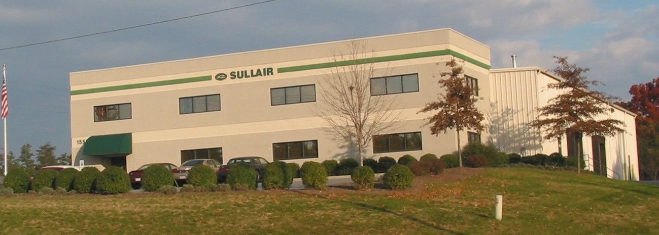 Two-story beige office building with green awnings and a small lawn in front