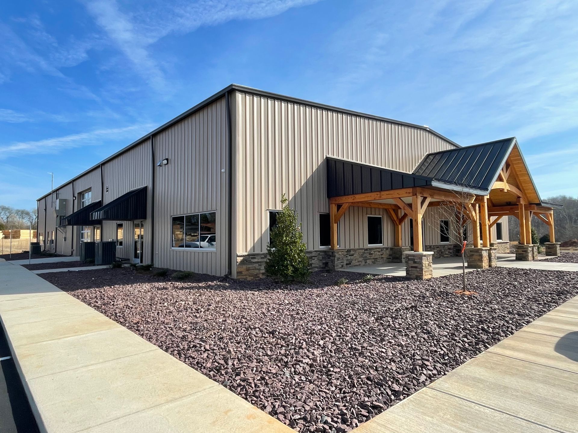Modern industrial building with metal siding, wood entry, and gravel landscaping under a blue sky
