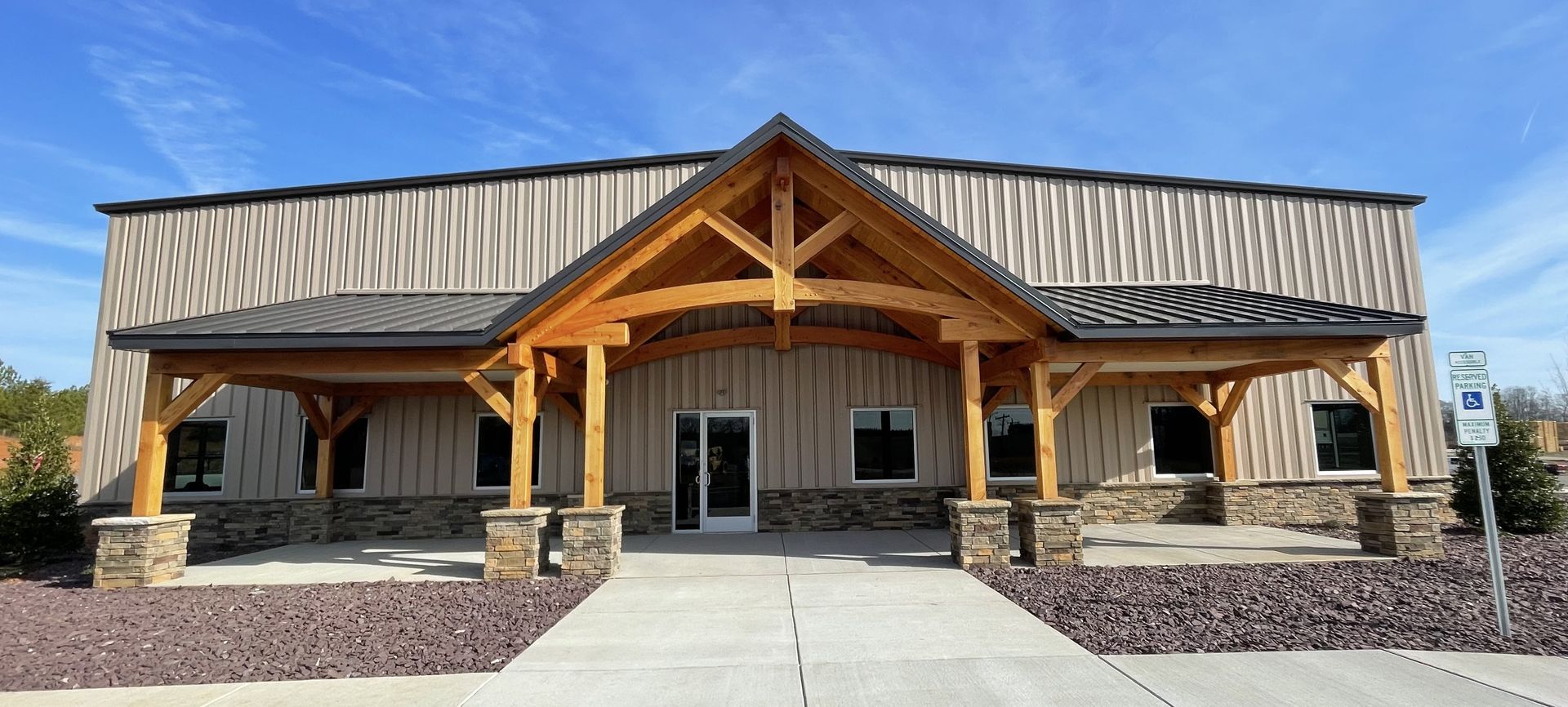 Front view of a rustic building with a metal roof, stone columns, and a central entrance walkway