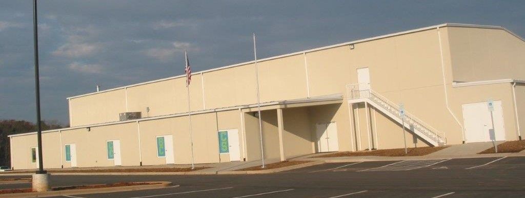 Beige industrial building with a curved roof and a row of small windows under a clear sky