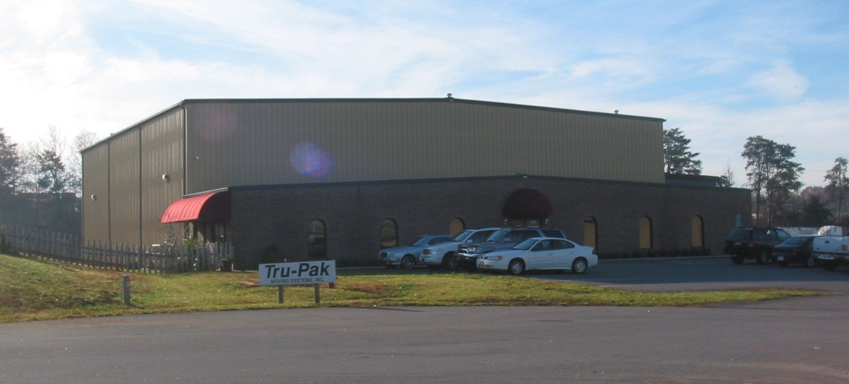 Low tan commercial building with a parked white car and a red flag by the roadside
