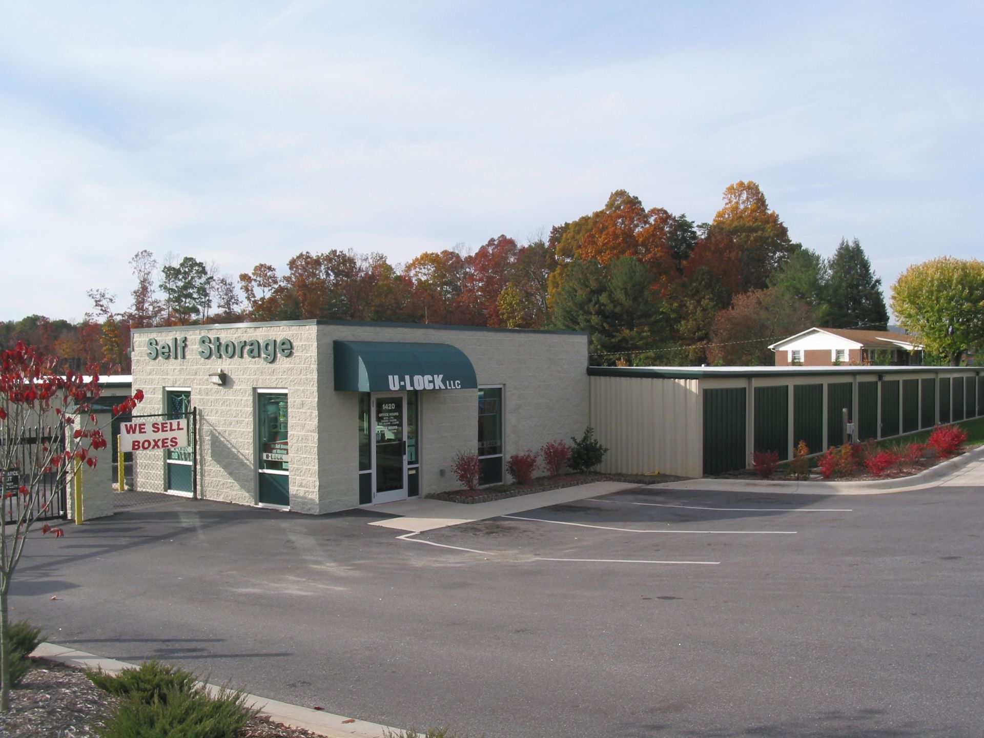 Self-storage facility with beige buildings and red autumn trees under a cloudy sky
