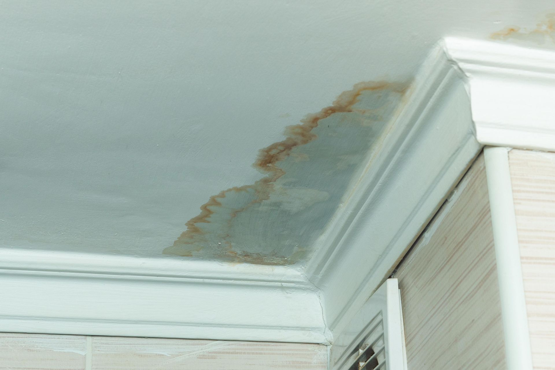 A corner of a ceiling in a house with signs of water damage and water stains. A corner of a ceiling in a house with signs of water damage and water stains.