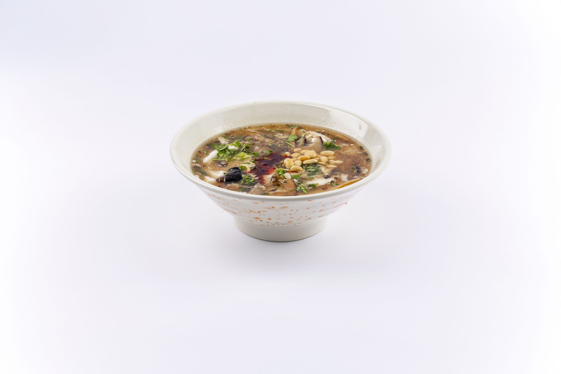A white bowl filled with hot and sour soup, garnished with herbs and fried toppings, isolated on a white background.