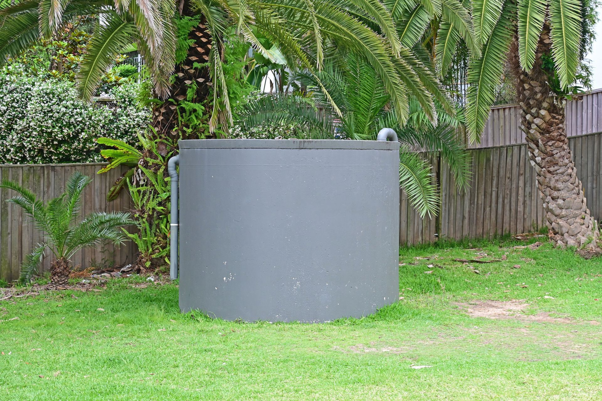 Grey concrete water tank in a park, surrounded by palm trees.