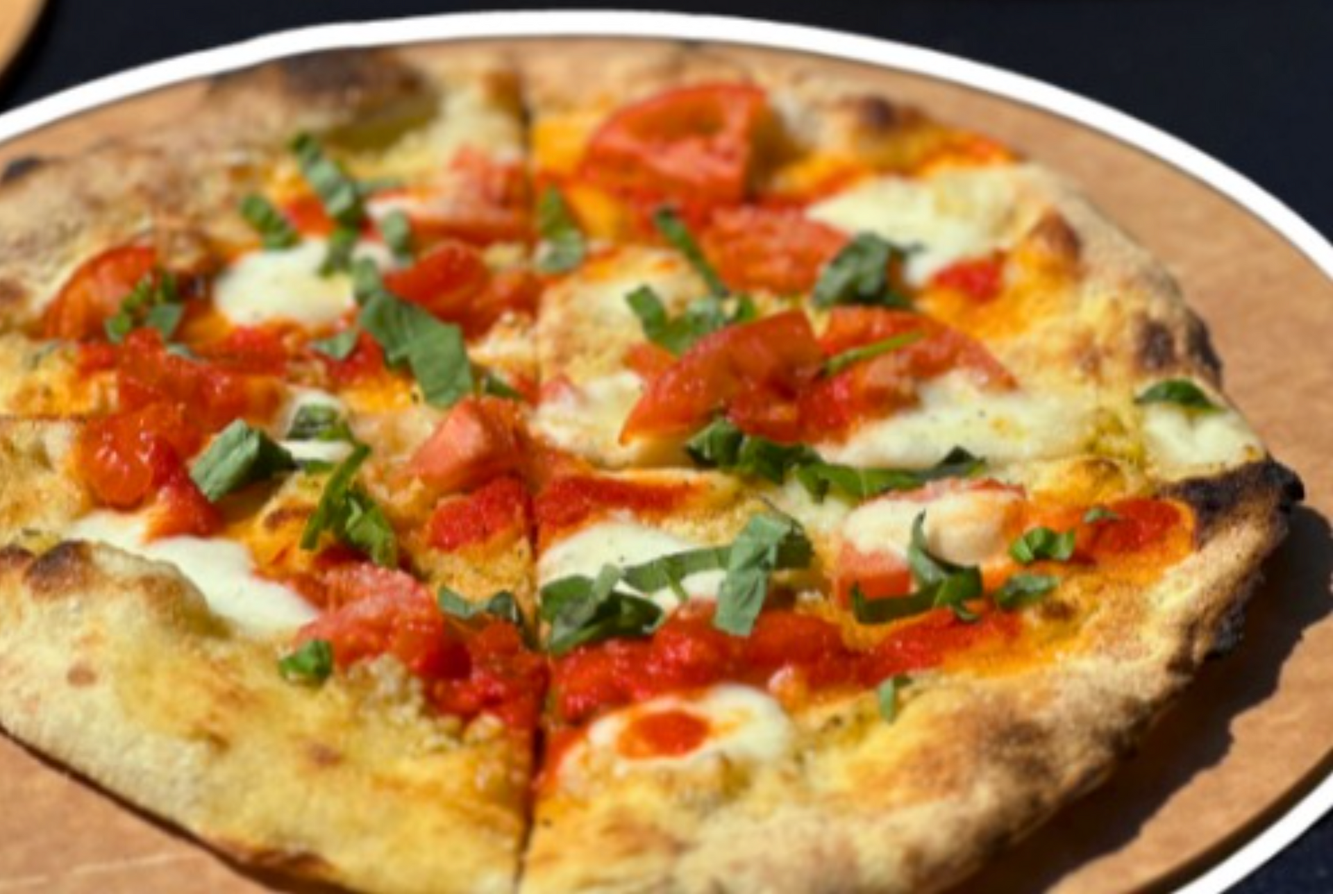 Pizza with tomato sauce, mozzarella, and basil, on a wooden plate.