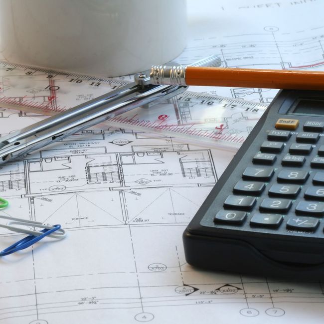 A calculator sits on top of a blueprint next to a pencil and compass