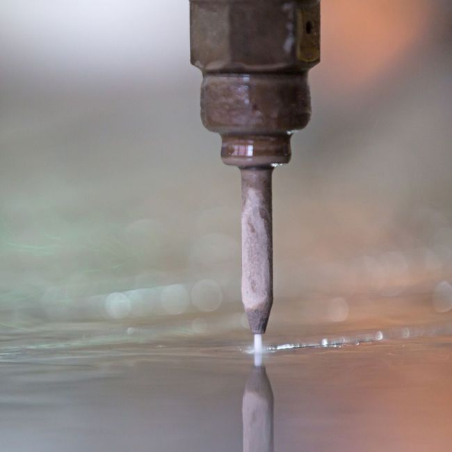 A close up of a water jet cutting a piece of metal.