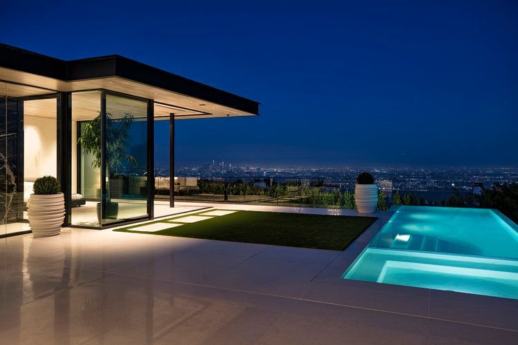 A modern house with a swimming pool and a view of the city at night.