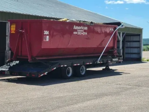 Person walking down a narrow alley beside green dumpsters and buildings on a sunny day