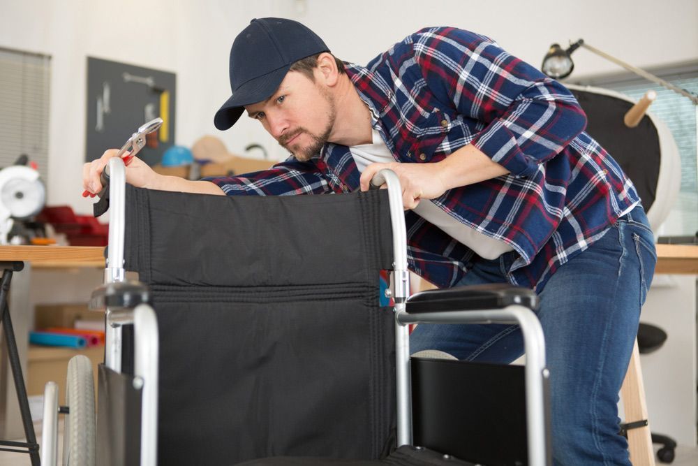 Man in cap and plaid shirt inspecting a wheelchair, indoor setting, focused expression.