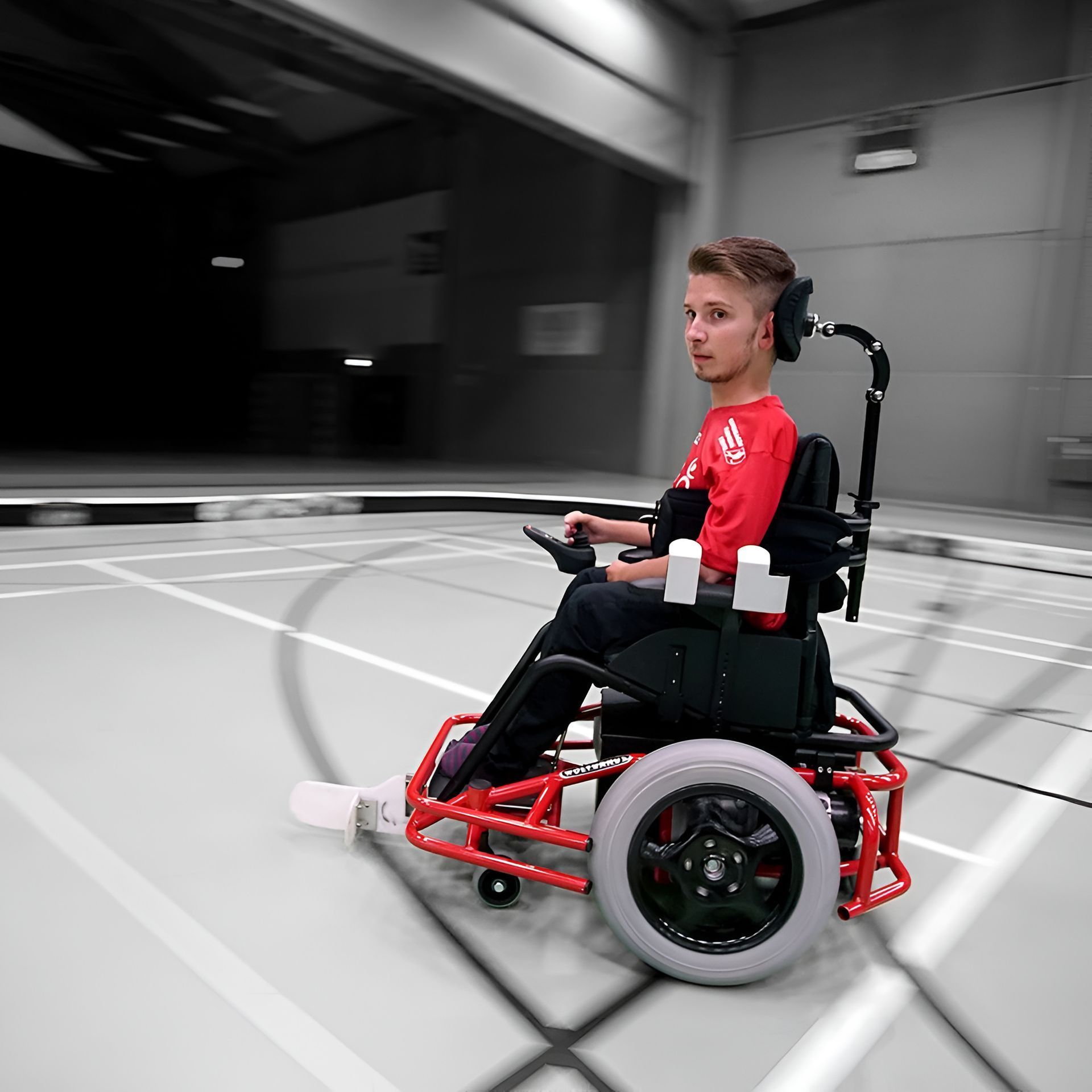 Young person in red shirt using a red sports wheelchair on a court.