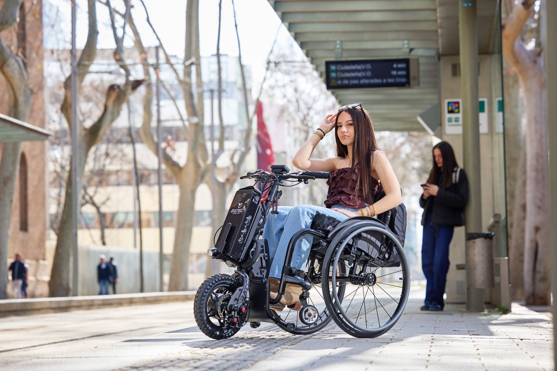 Woman in a wheelchair using a mobile device on a covered walkway