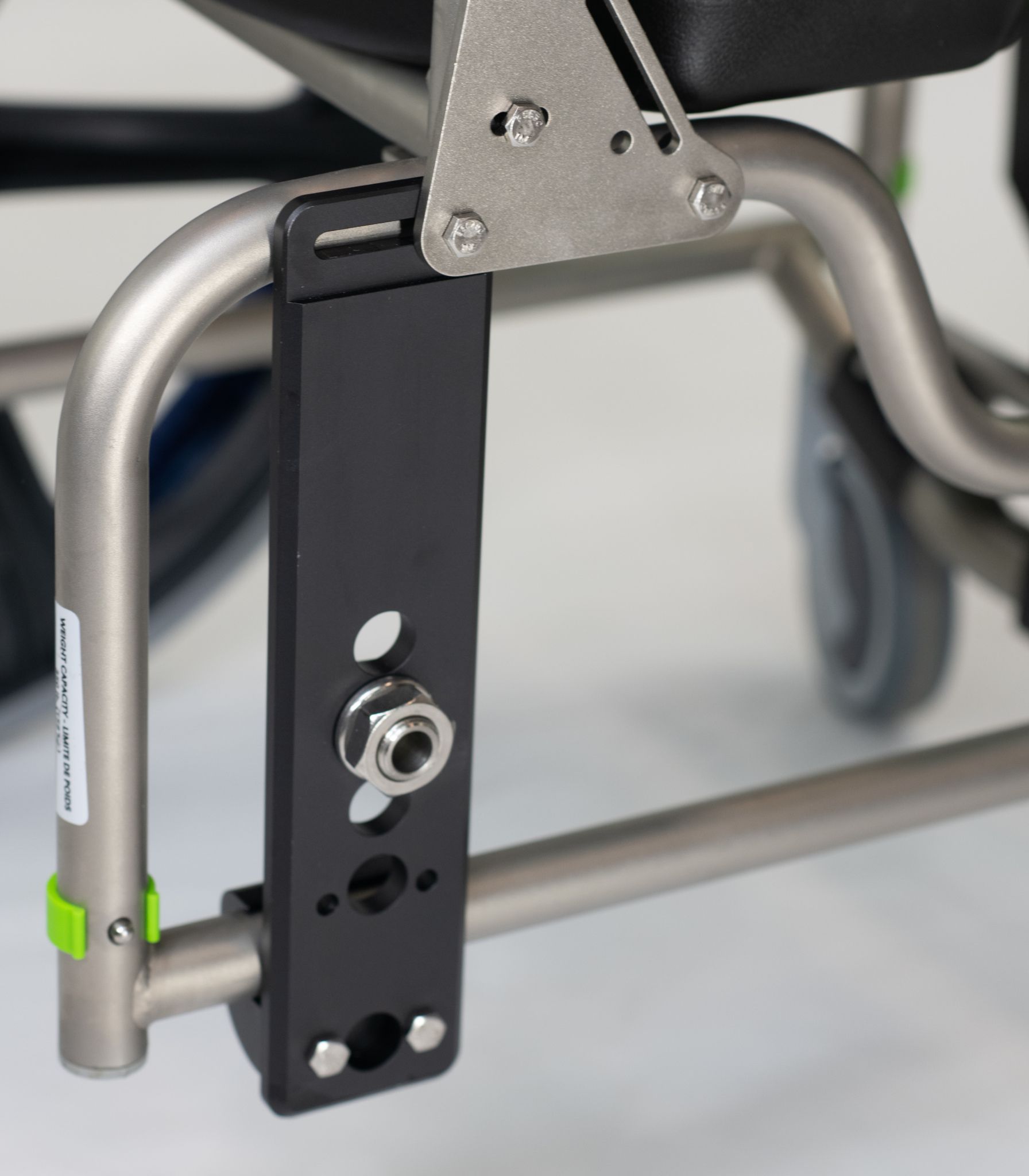 Close-up of a black wheelchair component attached to the frame with bolts and a wheel axle.